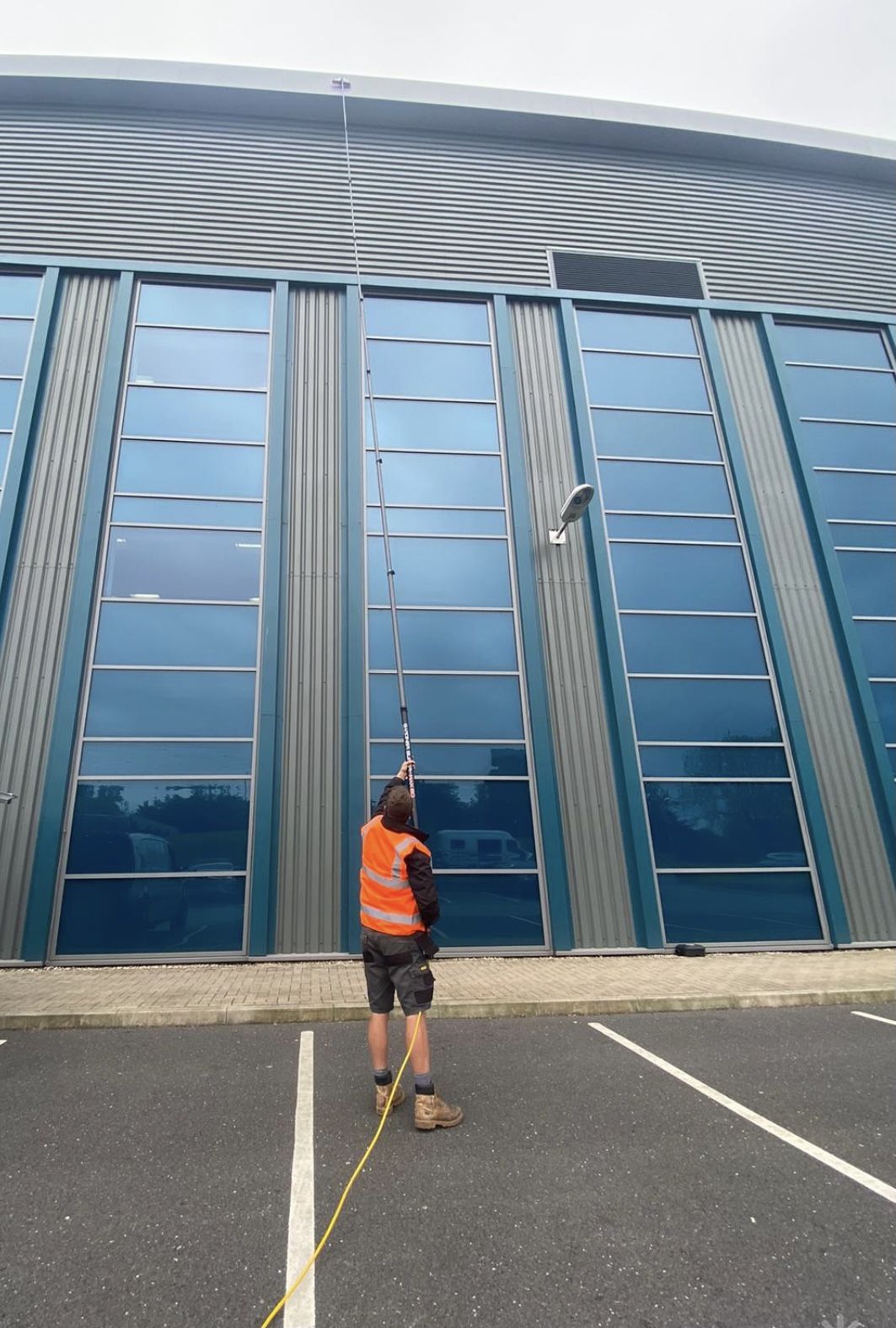 A cleaner in hi-vis using a water-fed pole on the glass front of a commercial unit
