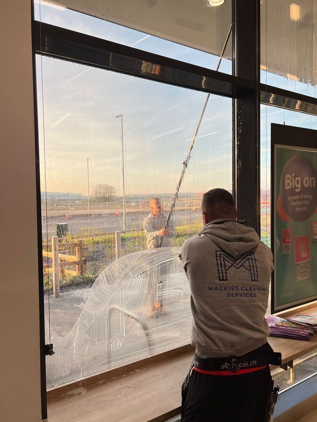 A cleaner using a squeegee on the inside of a shop’s front glass