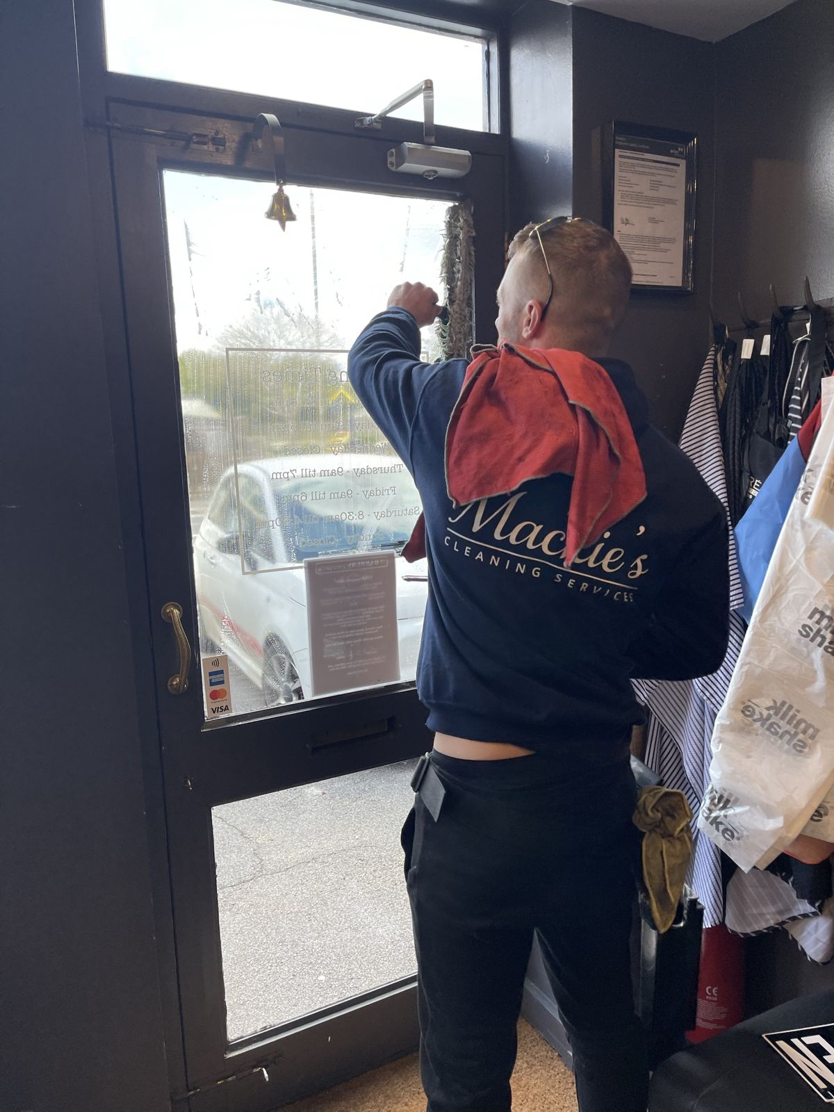 A cleaner in a branded hoodie cleaning the glass of a shop door from the inside