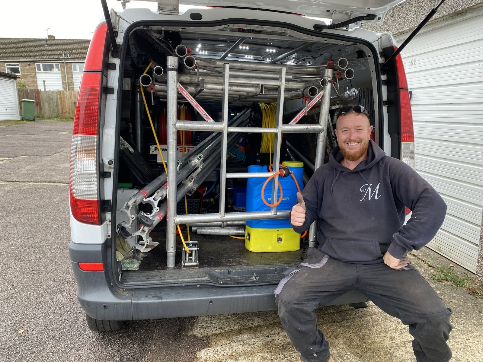 A cleaner sitting on the back of a van full of scaffold, thumbs up